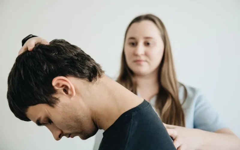 A physiotherapist helps a patient with neck exercises in a clinic setting.