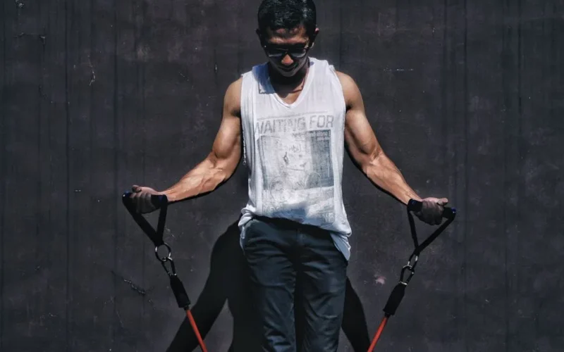 A muscular man using resistance bands outdoors for a fitness workout.