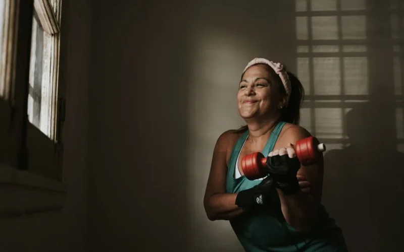 Confident middle-aged woman lifting dumbbells indoors, embracing a healthy lifestyle.