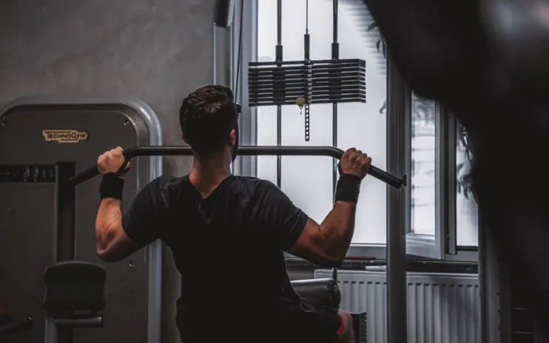 Back view of a man exercising with lat pulldown machine in the gym.