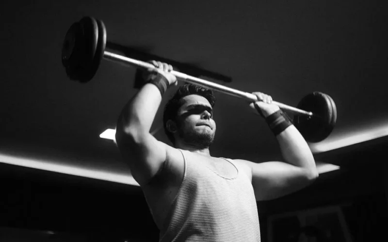 Black and white photo of a muscular man weightlifting indoors, showing strength and determination.
