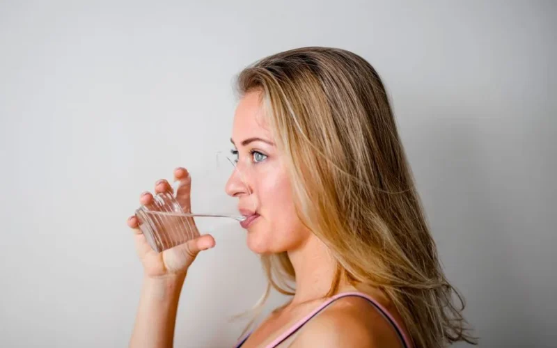 Side view of a woman with blonde hair drinking water from a clear glass.