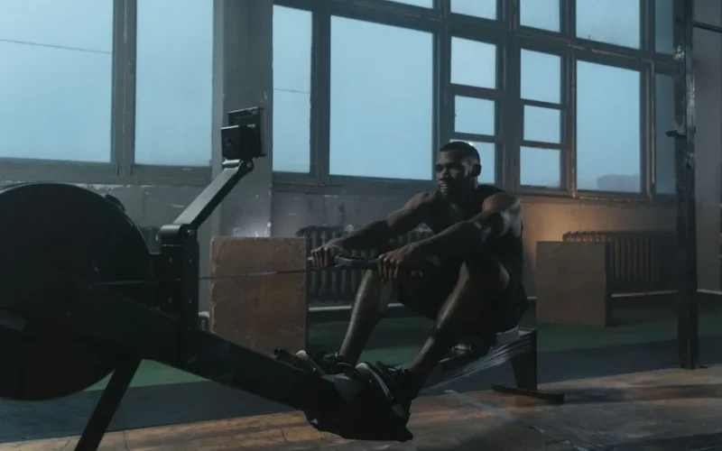 Focused athletic man working out on a rowing machine in a dimly lit gym setting.