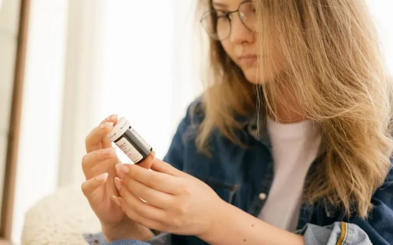 A woman carefully examines a medication bottle indoors, emphasizing health care attention.