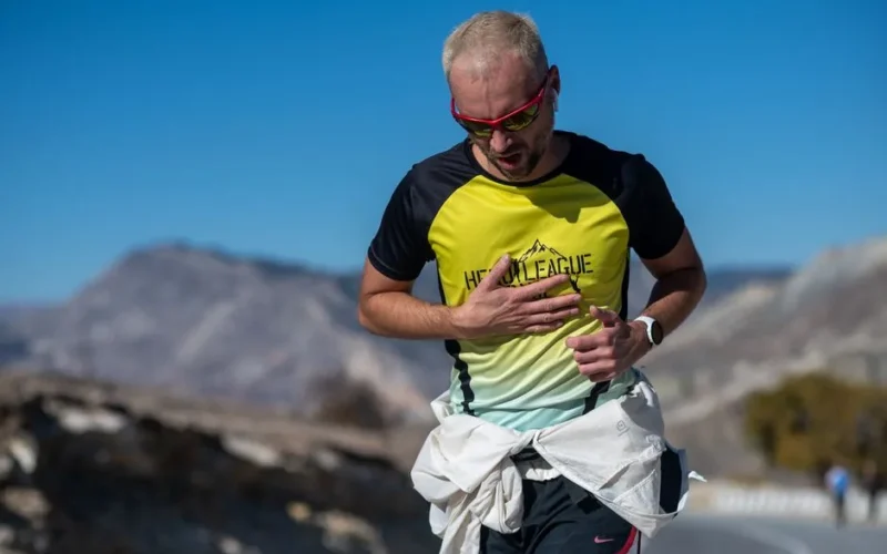 A man running on a mountain road in sunglasses and sportswear on a clear day.