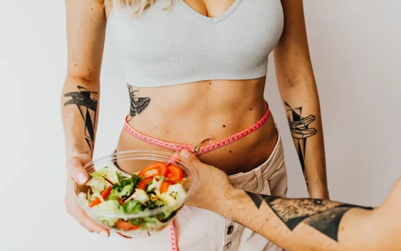 Fit woman measuring waist while holding a healthy salad bowl