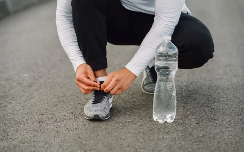 Runner tying shoelaces on the road with a water bottle beside. Fitness preparation.