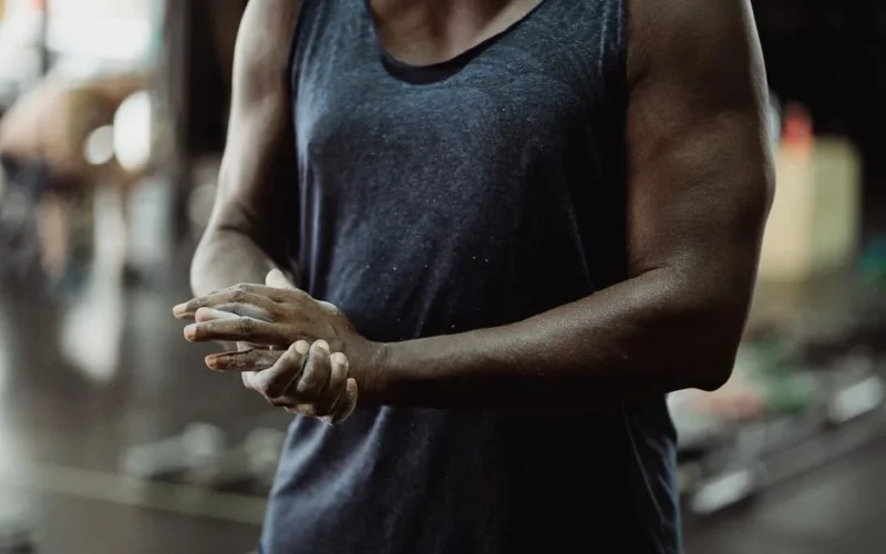 Close-up of a muscular man in a gym, focused on chalking hands for strength training.