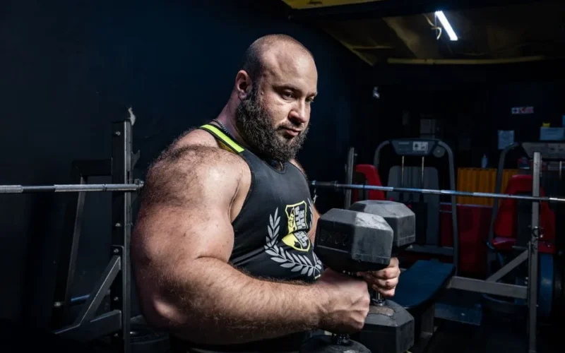 Strong bodybuilder lifting heavy dumbbells in a gym setting, showcasing strength and power.