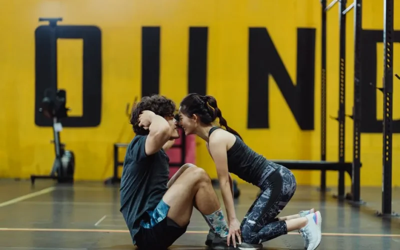Smiling couple doing sit-ups face to face in a modern gym.