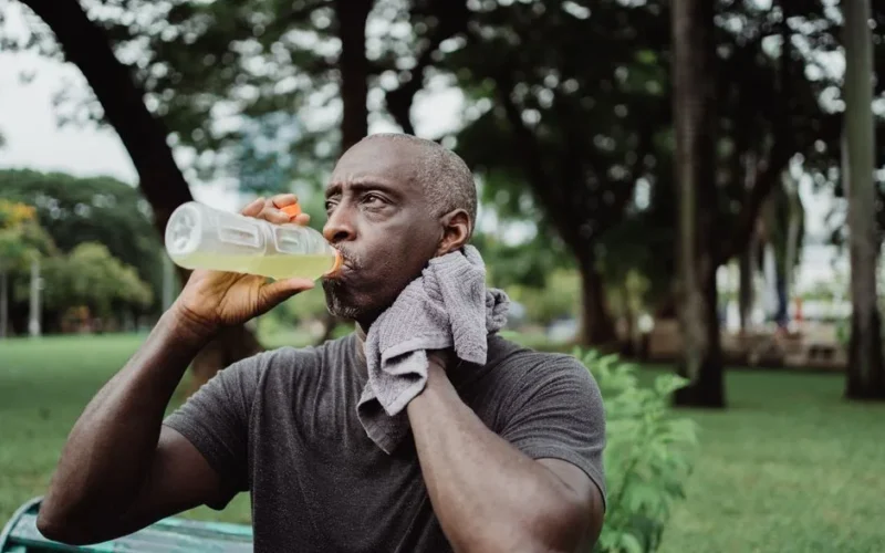 Adult man drinking sports beverage and wiping sweat in a park.