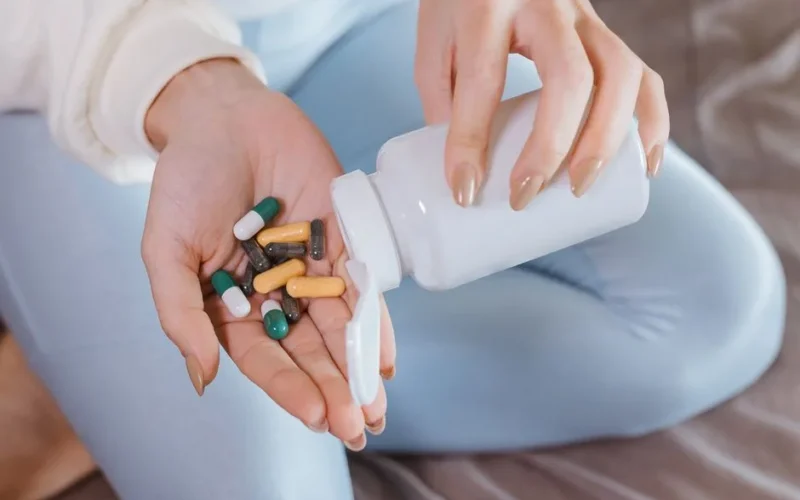 Close-up of hands pouring mixed capsules from a pill bottle indoors, focusing on healthcare and medicine.