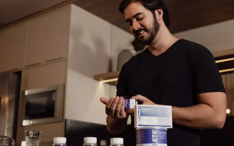 Man in kitchen holding and reviewing a bottle of supplements, indicating health-conscious lifestyle.