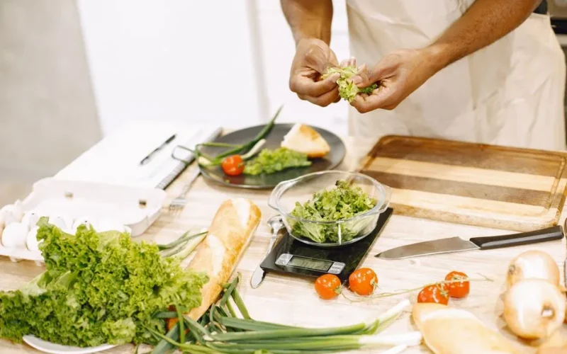 Person preparing fresh salad with tomatoes and baguette in kitchen setting.