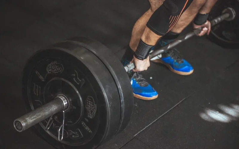 A man performing a deadlift with a heavy barbell in a gym setting, showcasing strength and fitness.