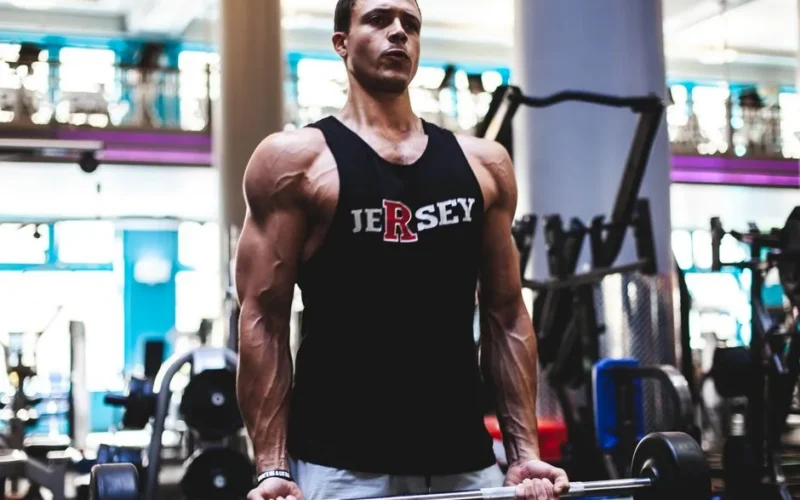 Fit man in a gym lifting barbell, showcasing strength and fitness in activewear.
