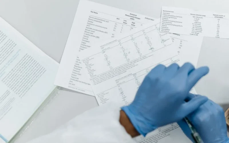 Close-up of gloved hands reviewing printed lab test results on a white surface.