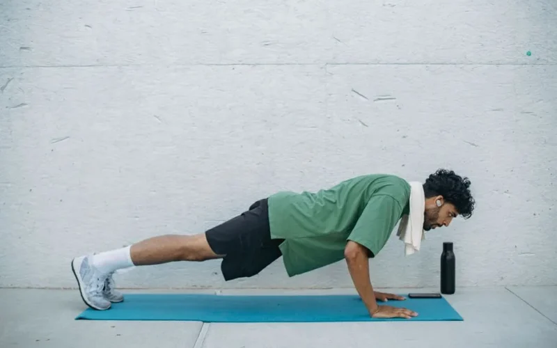 Adult man doing push-ups on yoga mat indoors, exemplifying healthy lifestyle and fitness.
