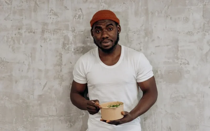 Smiling man in a white t-shirt enjoying a healthy meal indoors, embodying a fit lifestyle.