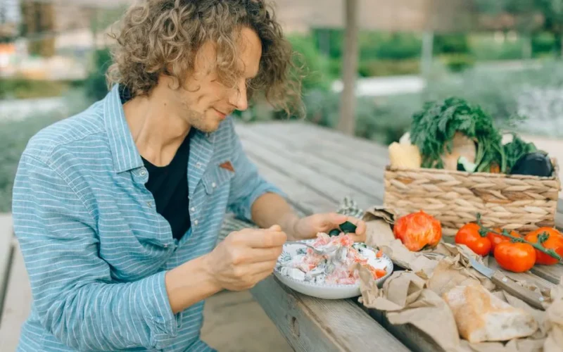 A man enjoying a healthy meal with fresh vegetables at an outdoor picnic table.