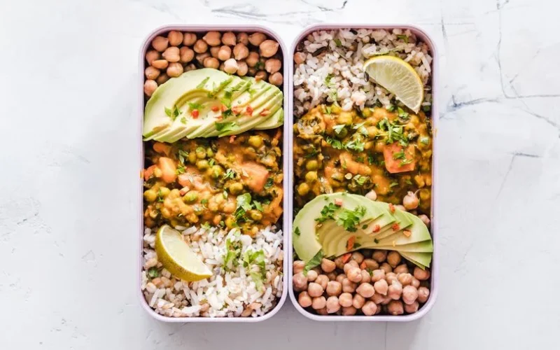 Delicious vegan lunchboxes featuring chickpeas, rice, avocado, and curry on a white background.