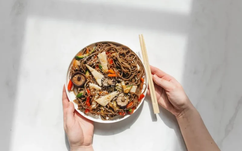 A vibrant dish of soba noodles with vegetables on a white background, captured in daylight.