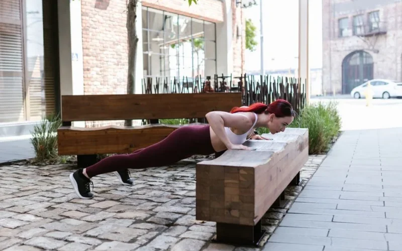 Woman performs push-ups on a wooden bench outdoors, showcasing fitness and active lifestyle.