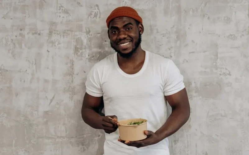 A happy man in a white shirt holding and enjoying a fresh salad indoors.
