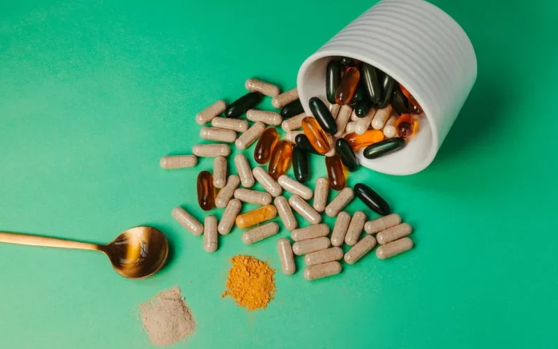 A mix of capsules, pills, and powder on green background with spoon.
