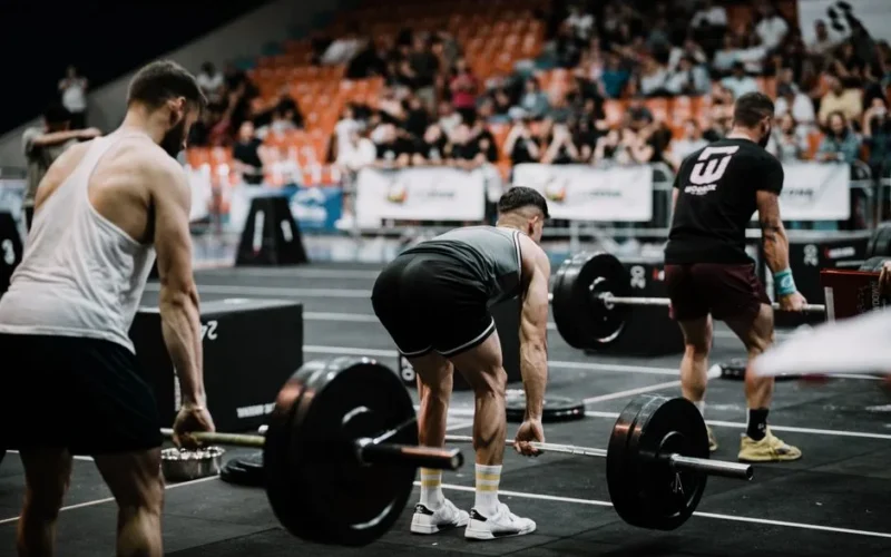 A group of athletes performing deadlifts during a competitive weightlifting event indoors.