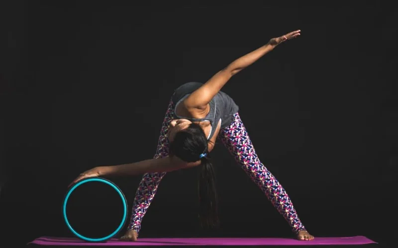 Adult woman performing yoga stretch with a yoga wheel in a studio setting.