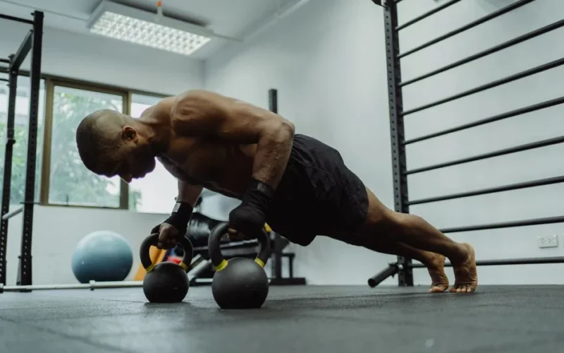 A fit man performs push-ups using kettlebells indoors, showcasing strength and fitness.