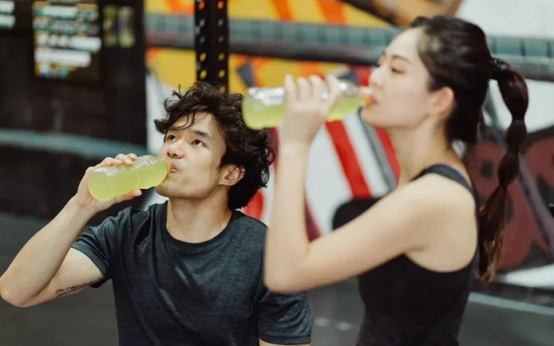 Fit Asian couple hydrating at the gym after an intense workout. Refreshing drink break.
