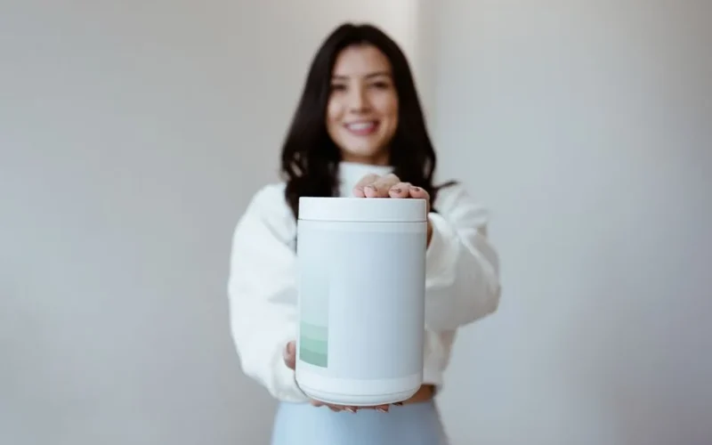Brunette woman smiling while holding a blank container, perfect for product mockup.