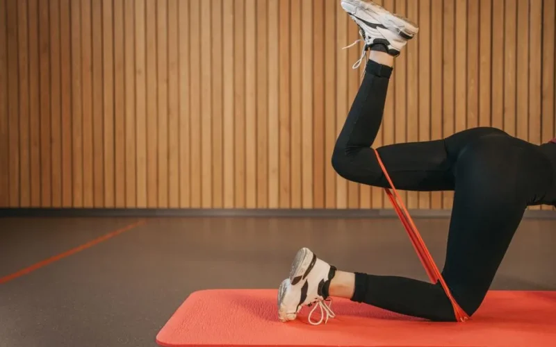 Woman in activewear working out indoors with resistance band on yoga mat, focusing on legs.