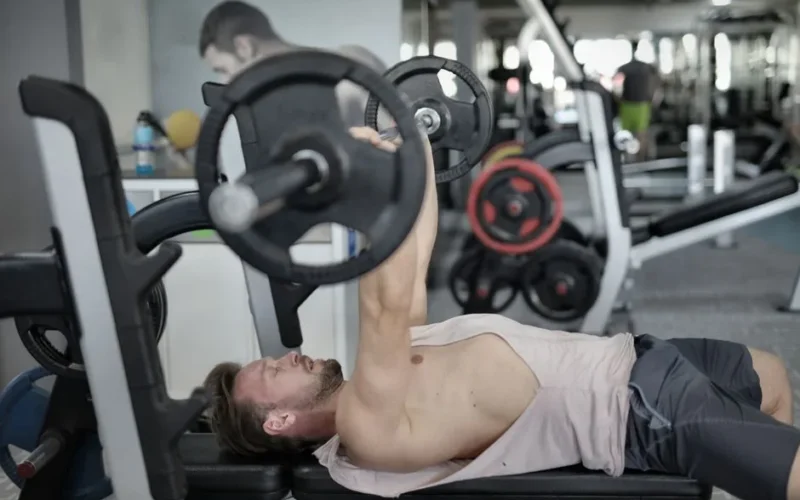 Side view of strong young sportsman in sportswear lying on bench and pressing heavy barbell doing chest exercise training in modern gym