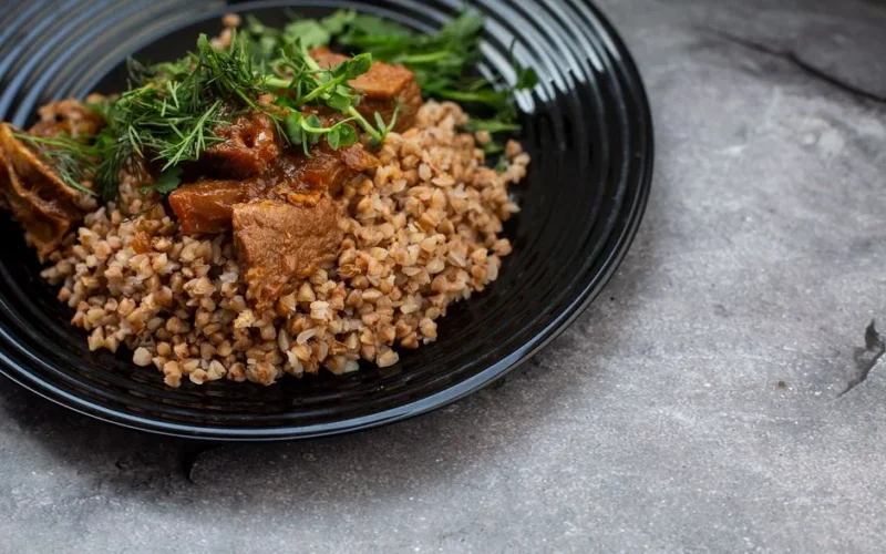 Delicious buckwheat with seasoned beef and greens served on a black plate.