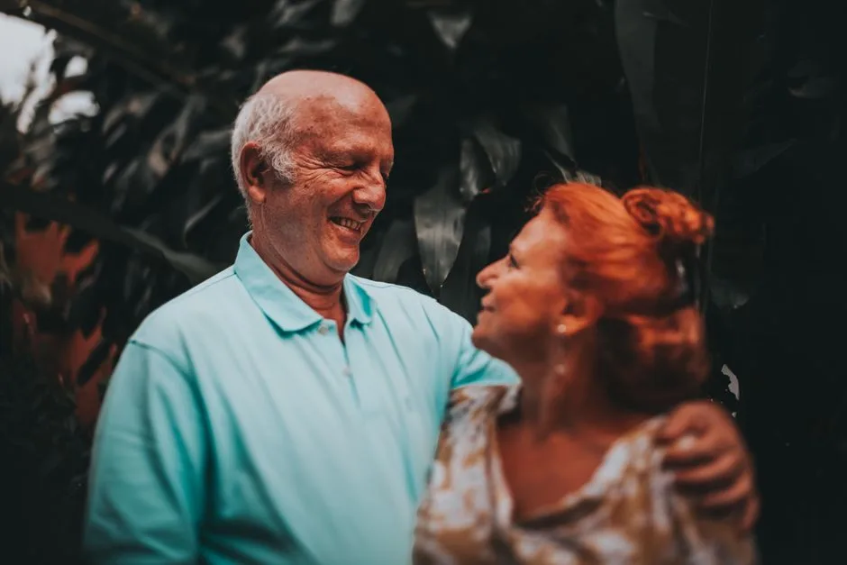 Elderly couple smiling and embracing in lush outdoor setting, capturing love and friendship.