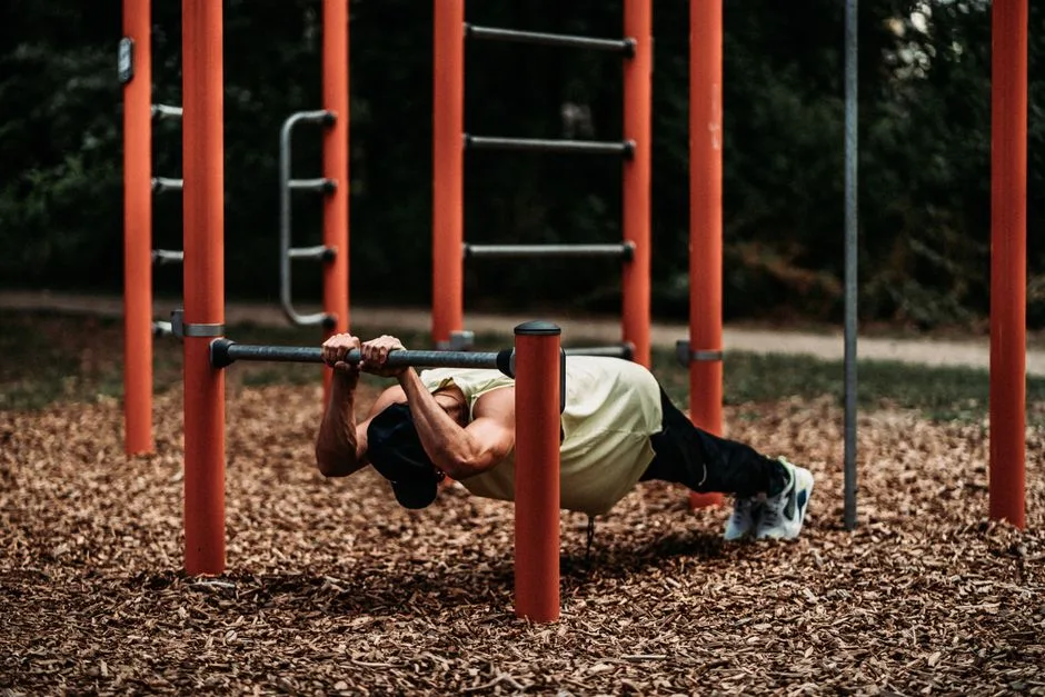 Strong man executes calisthenics on iron bars in a park, focusing on strength and balance.