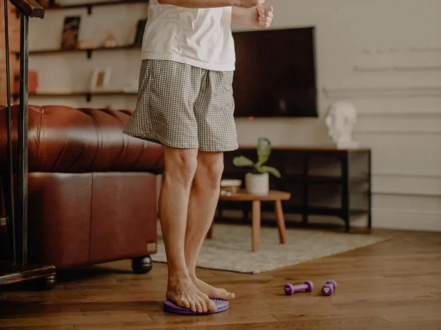 Man practicing balance exercise at home with a focus on legs and barefoot posture.