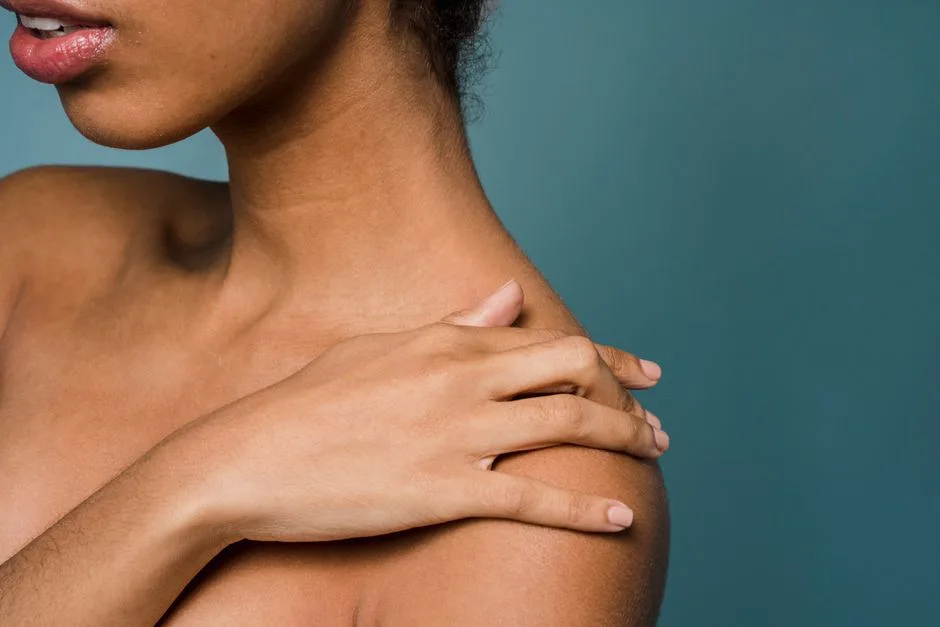 Side view of crop anonymous young graceful black female touching bare shoulder while standing against blue background