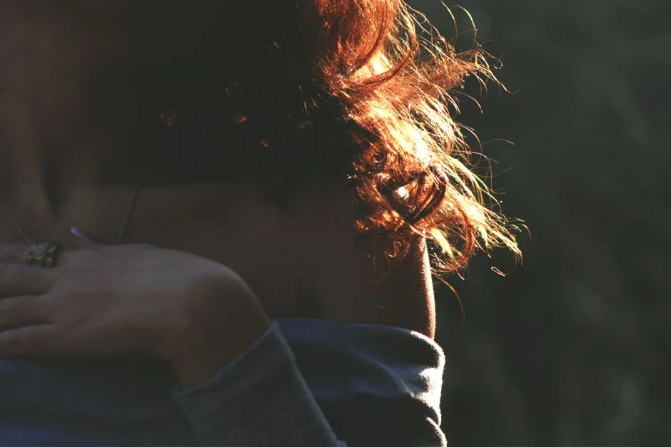An artistic shot highlighting a woman's backlit curly hair and shoulder, emphasizing light and shadow.