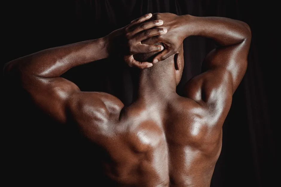 Rear view of a shirtless muscular man flexing his biceps, showcasing strength and fitness.
