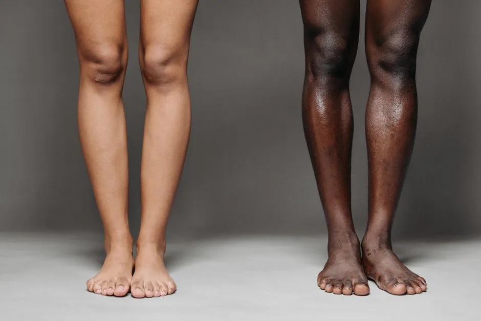 Image of two pairs of diverse bare legs standing against a gray background, showcasing skin tone variety.