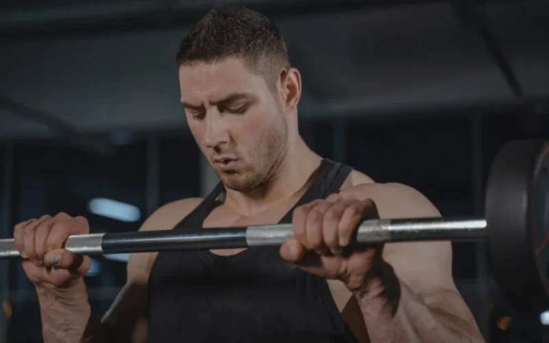 Muscular man lifting barbell during workout, showcasing strength and focus.