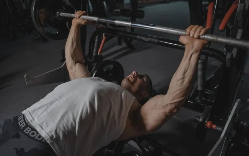 A focused man lifts heavy weights on a bench press machine in a dimly lit gym.