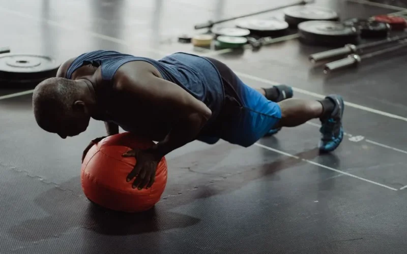 Adult man in gym doing push-up on a medicine ball, demonstrating strength and balance.