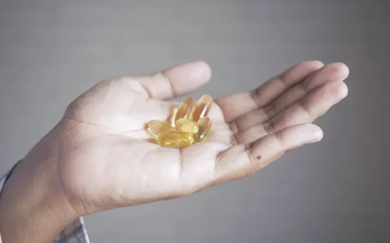 Hand holding yellow capsules, representing supplements and health care.
