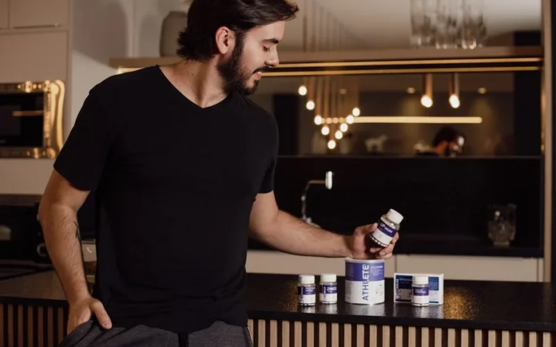 A man examines supplement bottles on a modern kitchen counter, reflecting a healthy lifestyle.