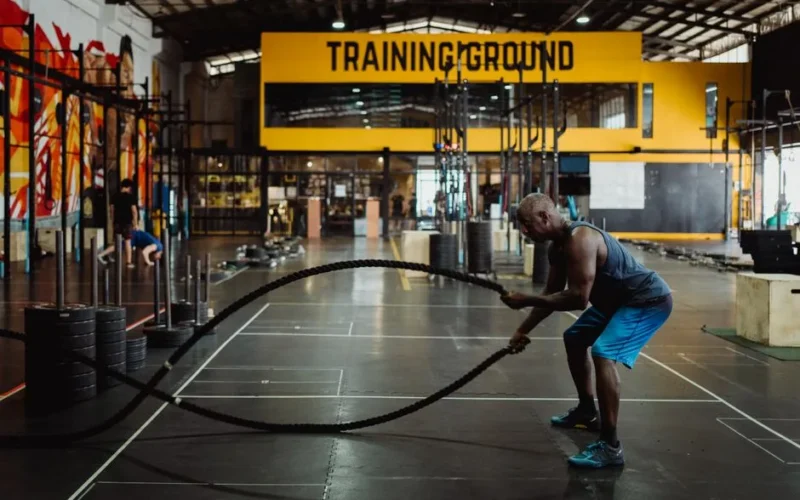 Athletic man engaging in a battle rope workout inside a modern gym setting for fitness training.